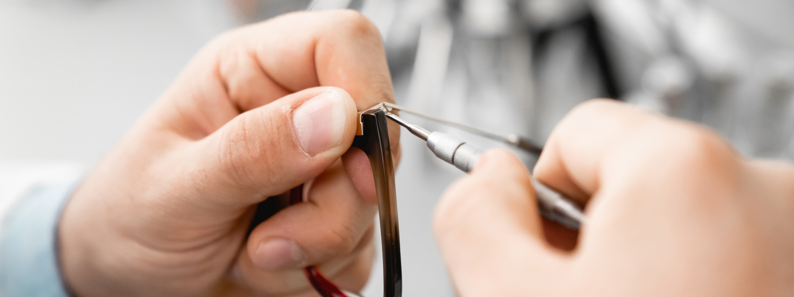 Zwei Hände halten eine Brillenfassung, die gerade mit angepasst wird.