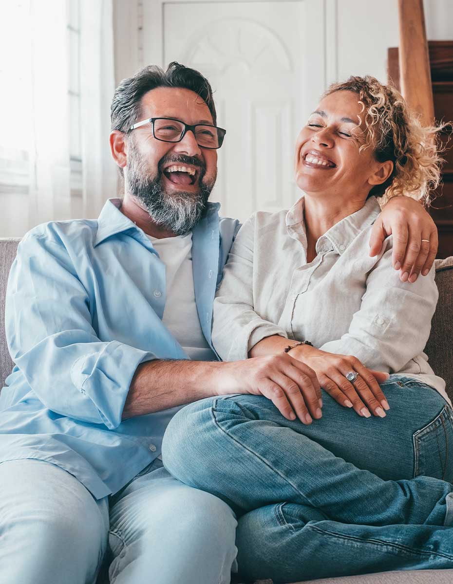 Glücklicher Mann mit Brille und lachende Frau sitzen auf einem Sofa